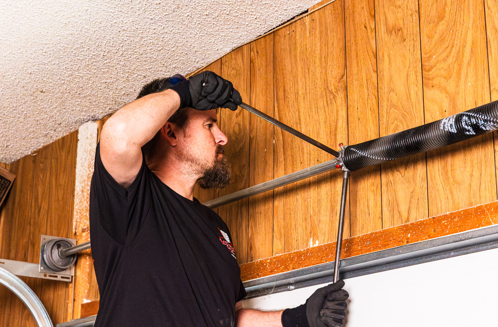 An experienced garage door fixer in Overland Park using a tool to fix a garage door spring.
