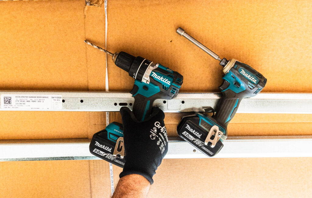 Two drills placed side by side against door. These are tools necessary for garage door maintenance in Shawnee.