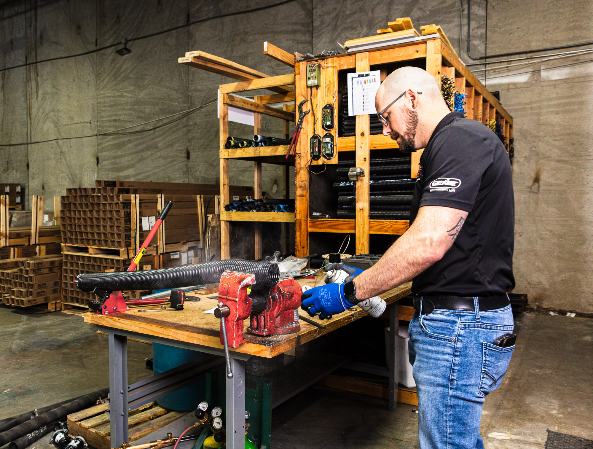 Garage door repairman in Shawnee working at a workshop bench, using tools to prepare and assemble parts for a garage door repair project.